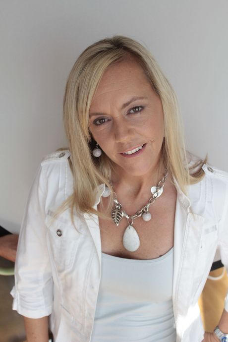 A woman wearing a white jacket and a necklace is smiling for the camera.