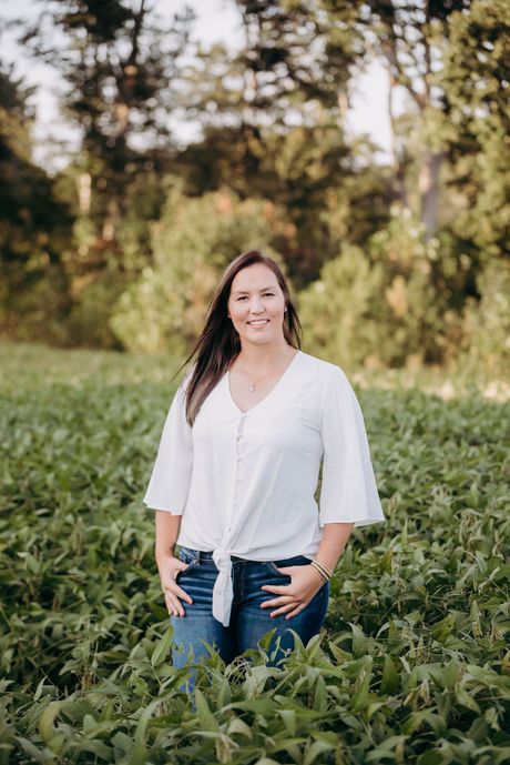 A woman in a white shirt and blue jeans is standing in a field of green plants.
