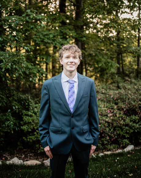 A young man in a suit and tie is standing in front of a forest.