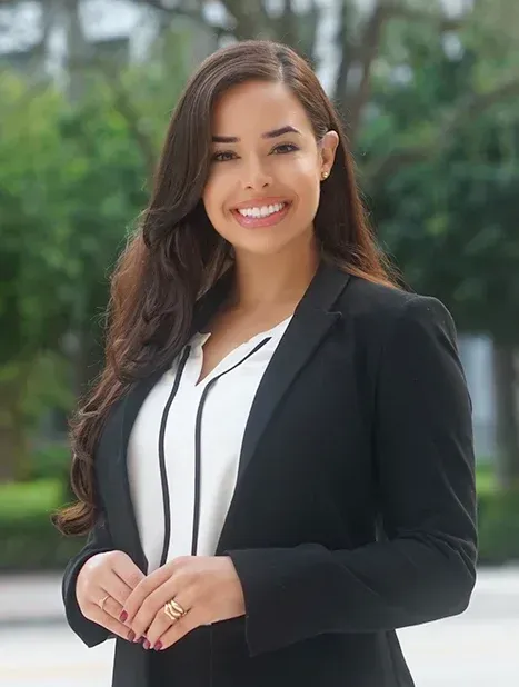Woman in black blazer and white top smiles outdoors.