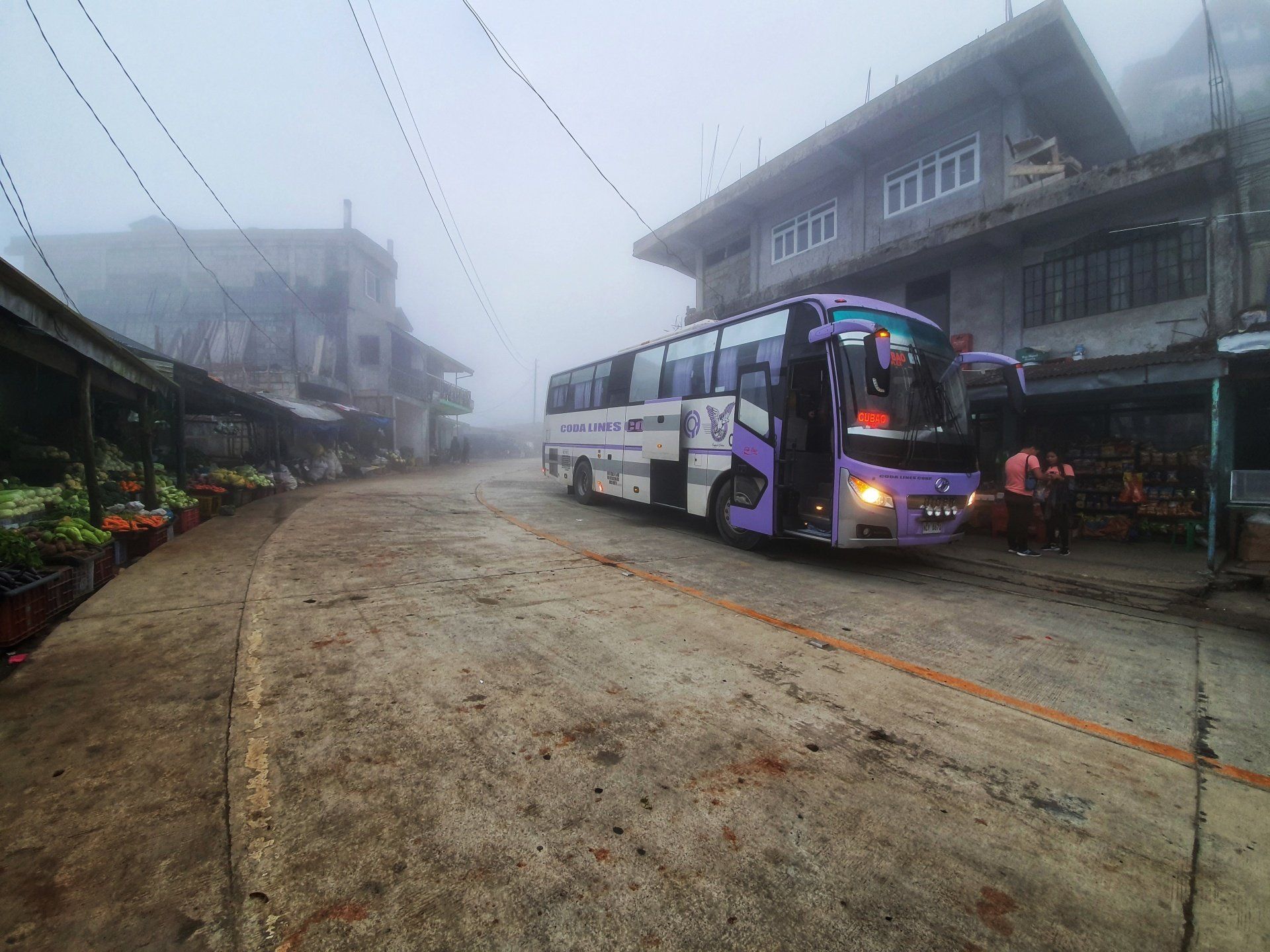 A bus is driving down a dirt road in the fog.