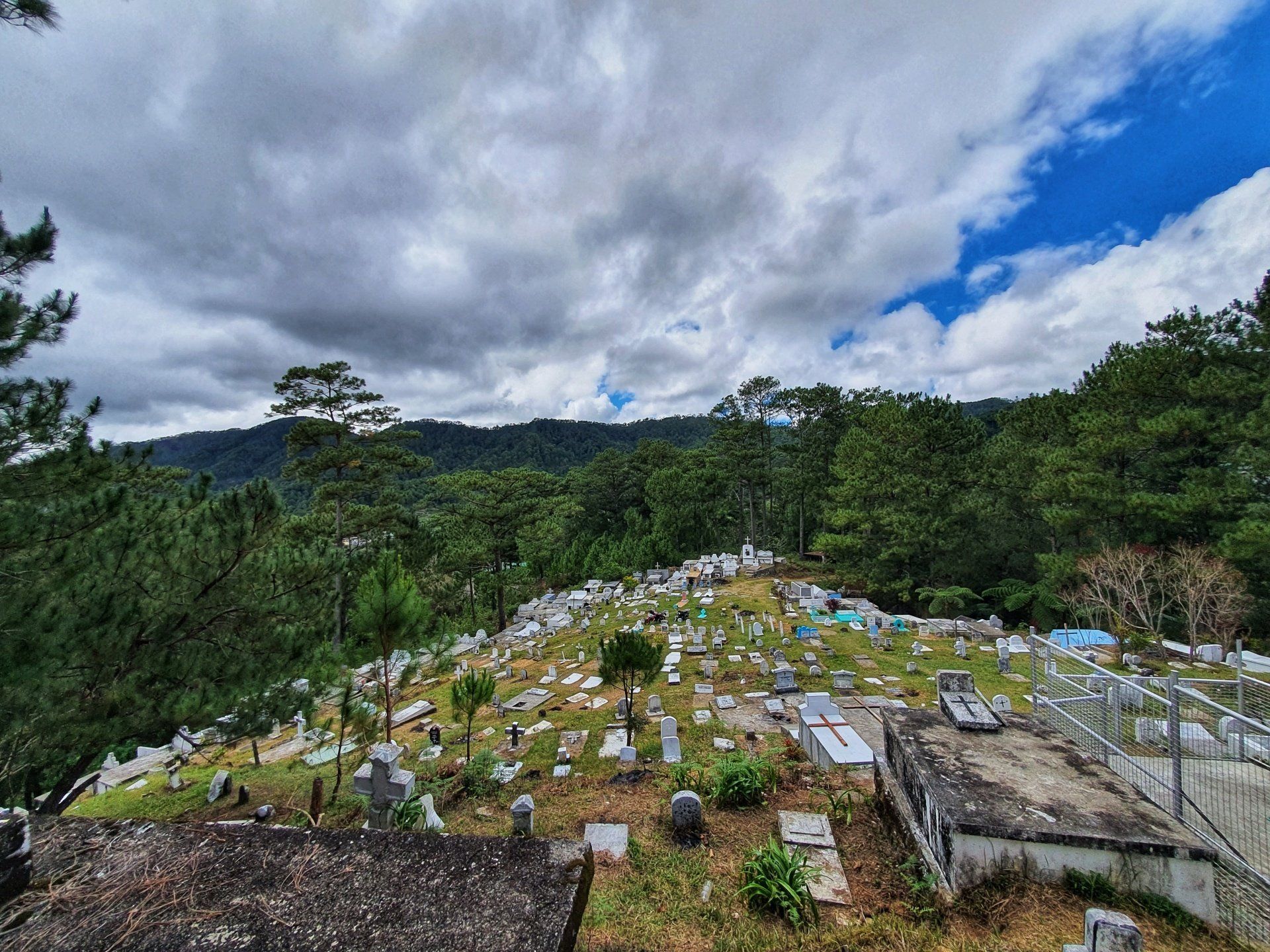 A cemetery surrounded by trees and mountains on a cloudy day.