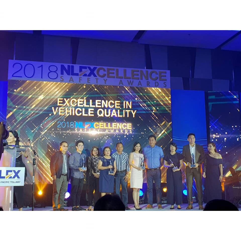 A group of people standing in front of a large screen that says excellence in vehicle quality
