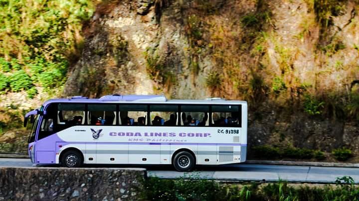 A purple and white cobra lines corp bus is driving down a road