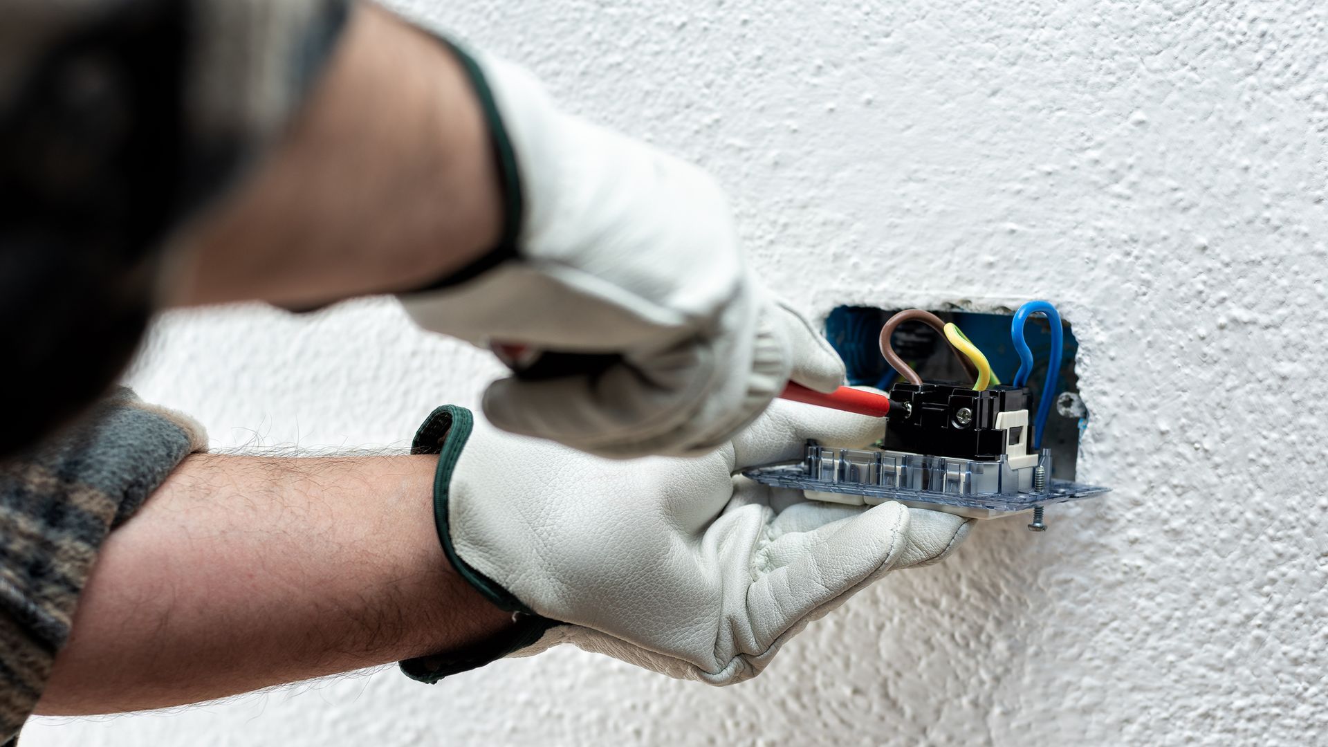 Electrician installing a power outlet on a white textured wall, wearing gloves. Electrician installing a power outlet on a white textured wall, wearing gloves.