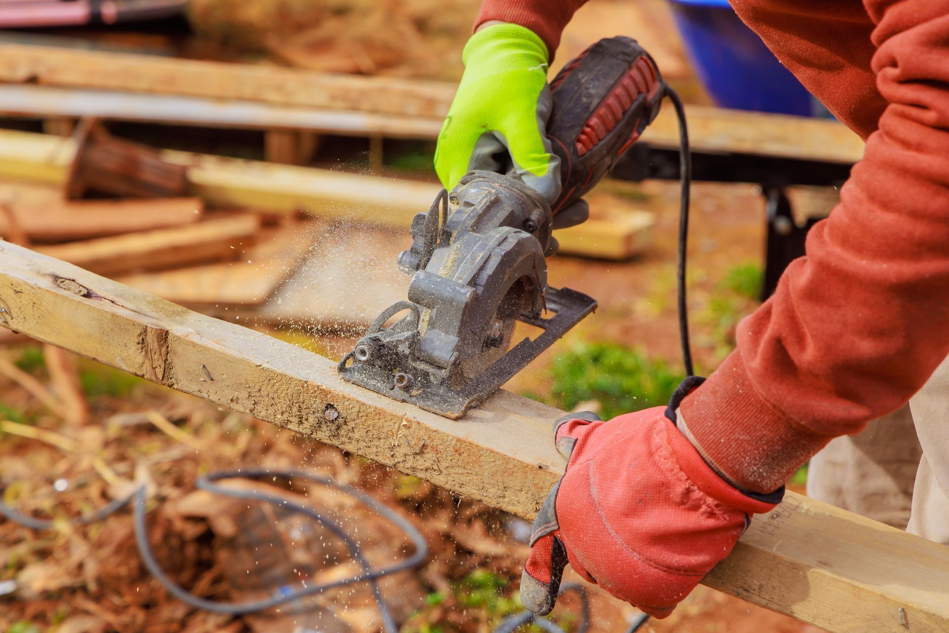 Person cutting wood with a circular saw, wearing red and green gloves. Person cutting wood with a circular saw, wearing red and green gloves.