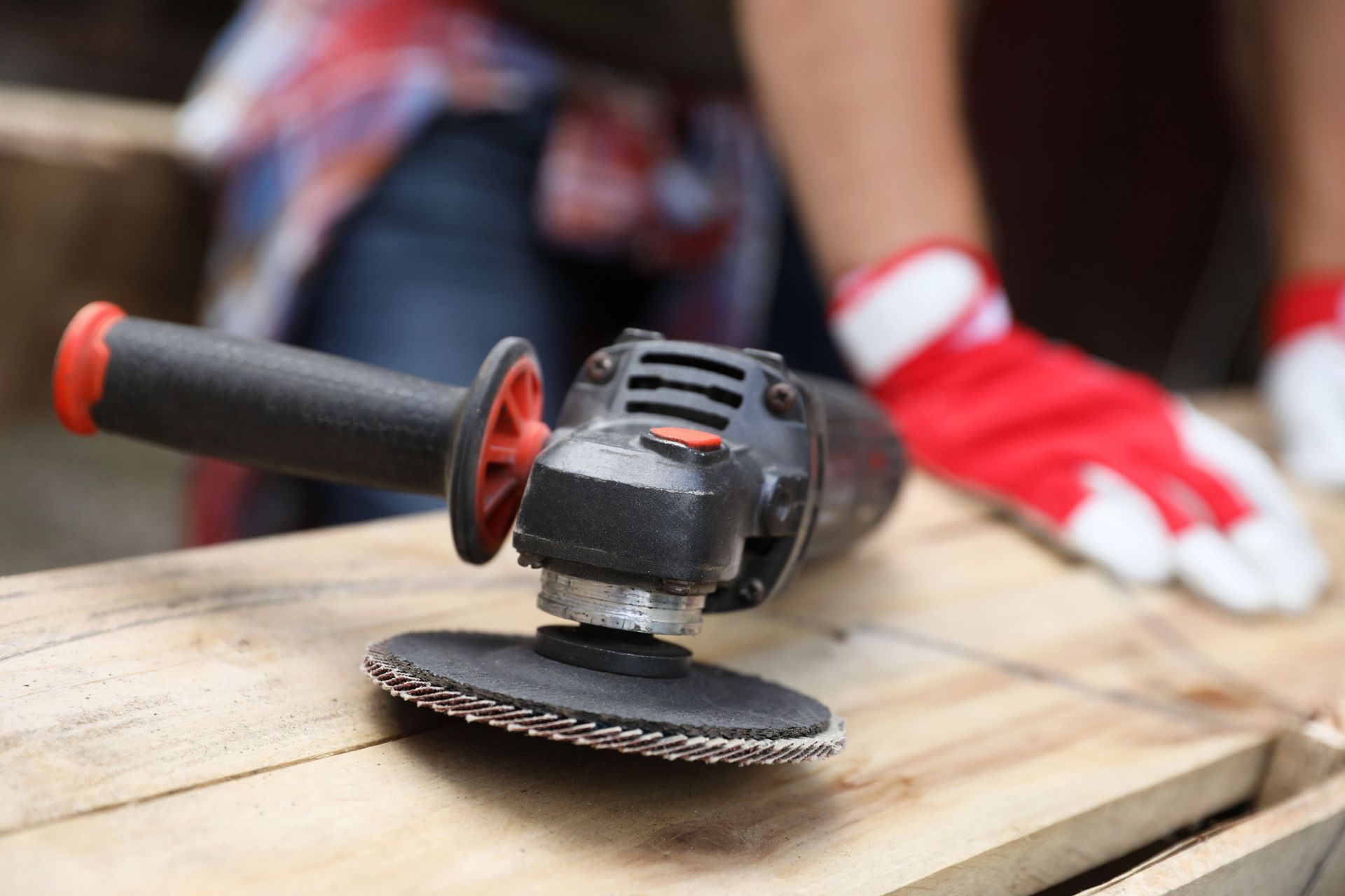 Angle grinder on wood, ready for use, with red-gloved hands in background. Angle grinder on wood, ready for use, with red-gloved hands in background.