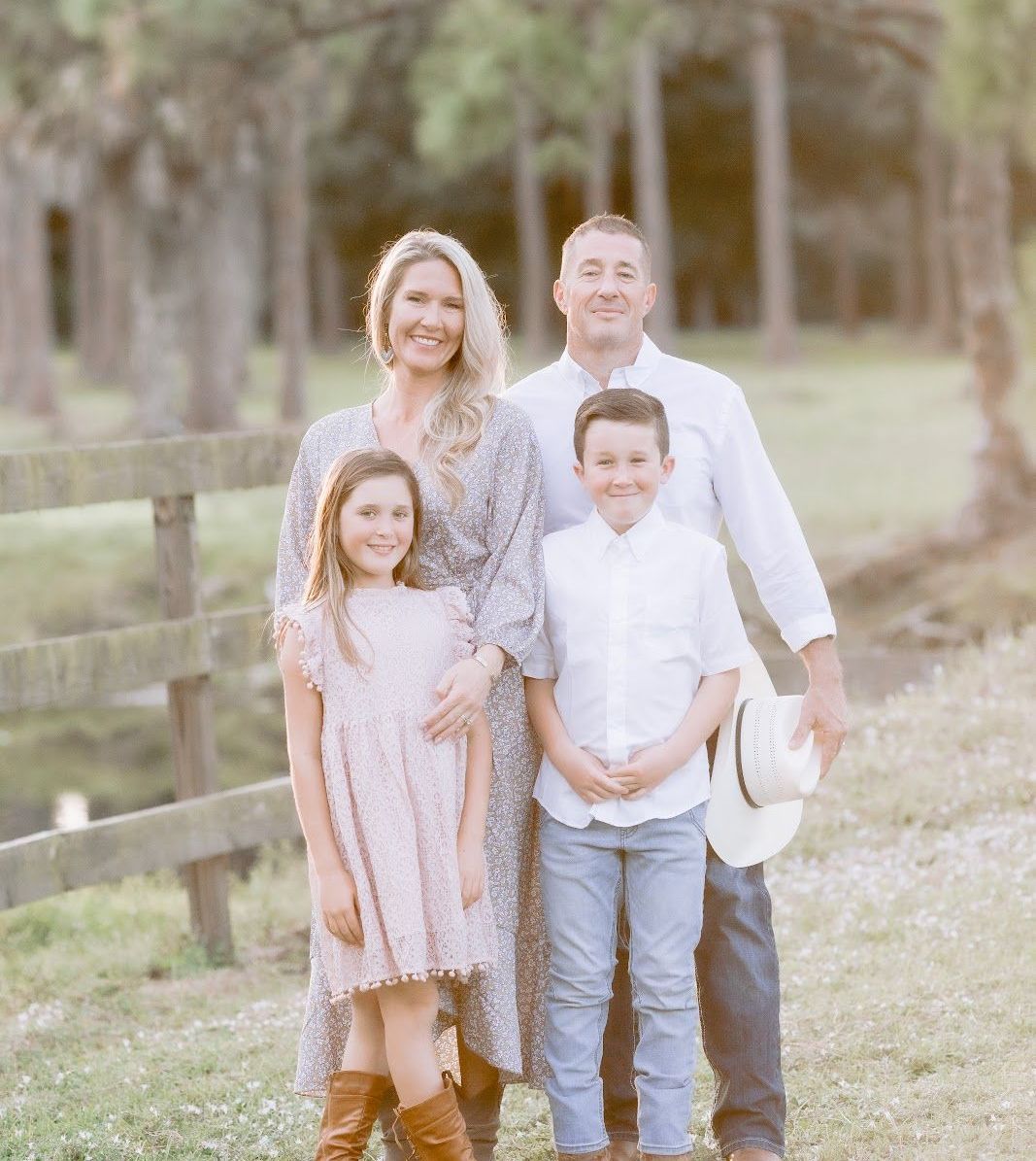 Family of four posing outdoors: mother, father, daughter, and son, near a fence.
