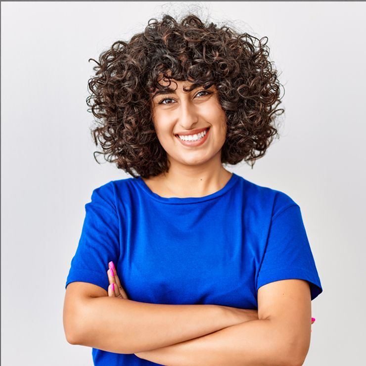 Woman with curly brown hair and a blue shirt smiles with arms crossed.