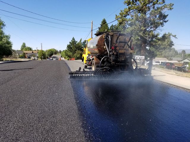 Road paving machine laying fresh black asphalt on a residential street under a clear blue sky