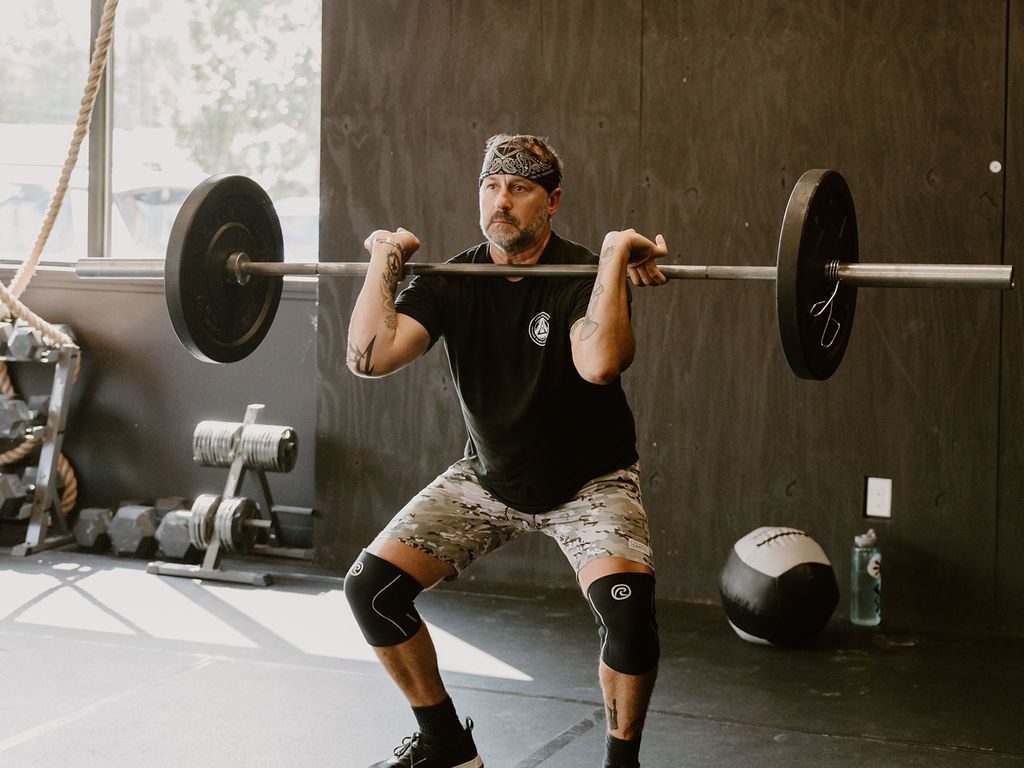 A man is squatting with a barbell over his head in a gym.