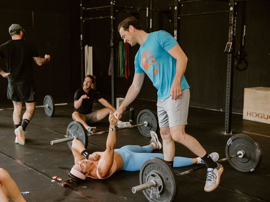 A man is helping a woman lift a barbell in a gym.