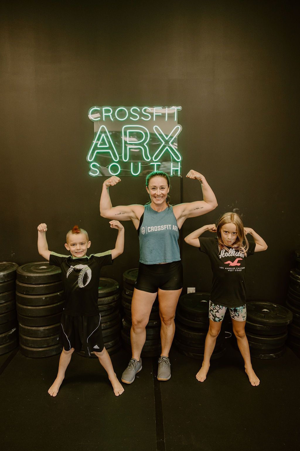 A woman and two children are flexing their muscles in a gym.