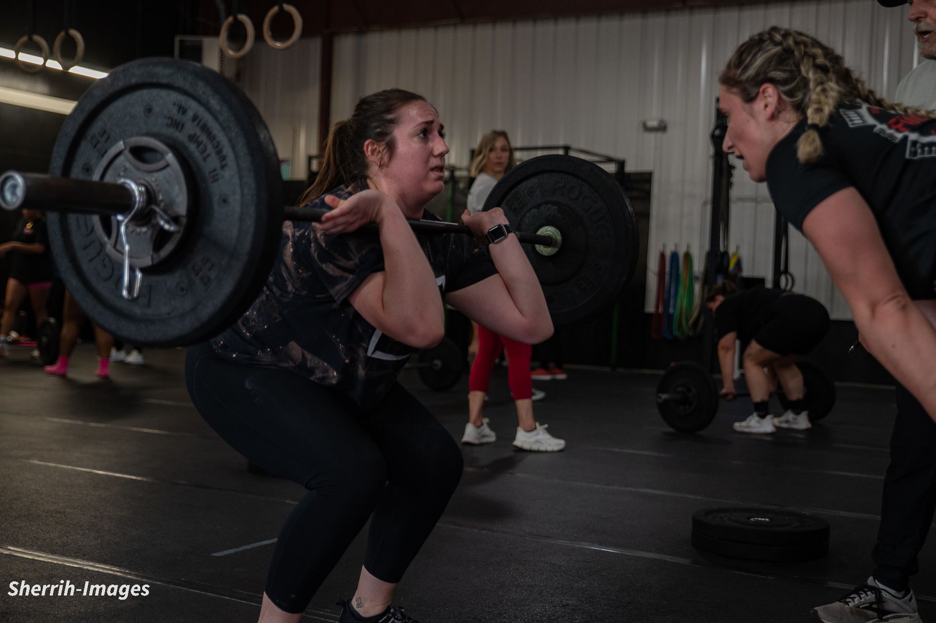 A woman is squatting with a barbell on her shoulders in a gym.