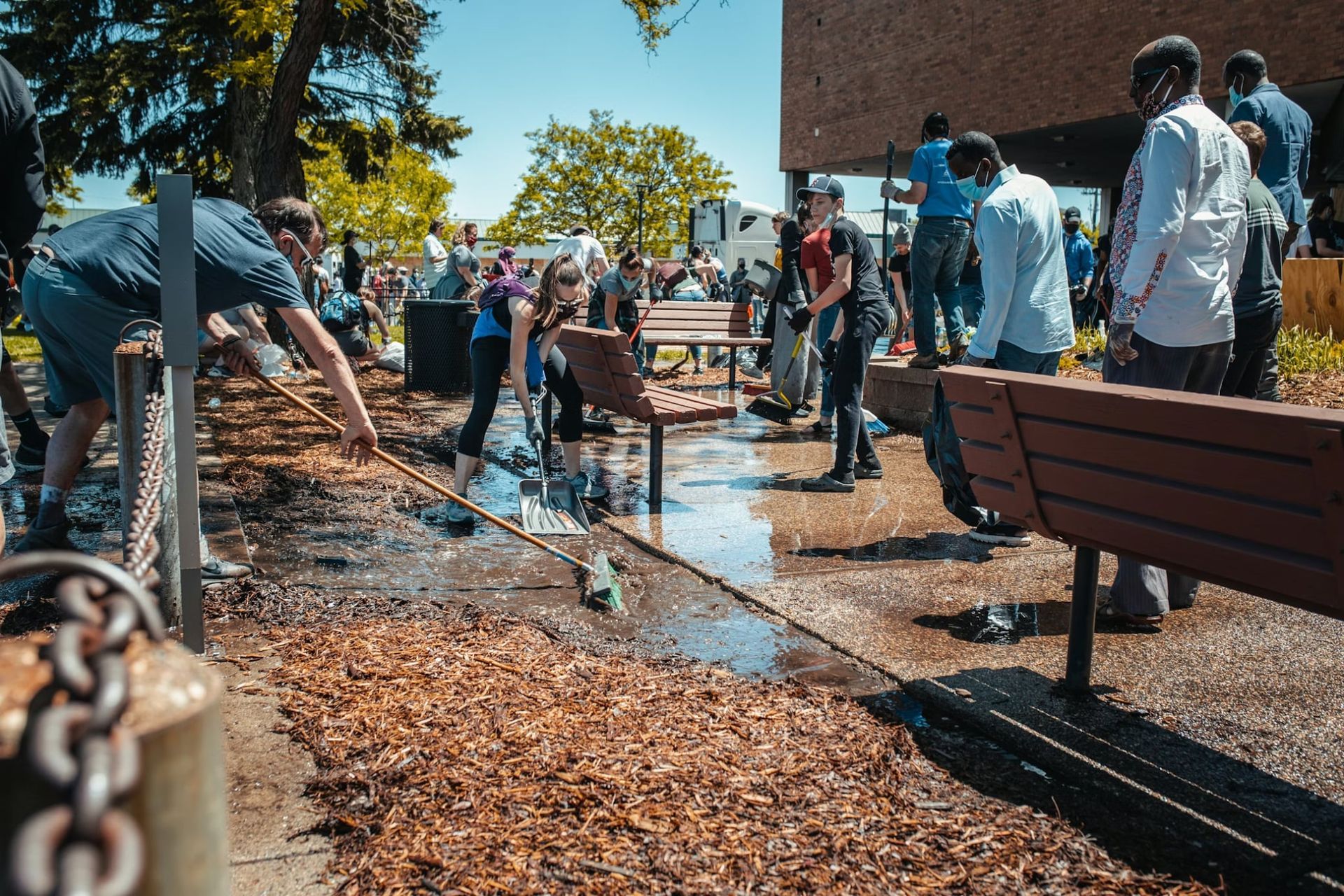 People cleaning up debris from a walkway near benches and a building.