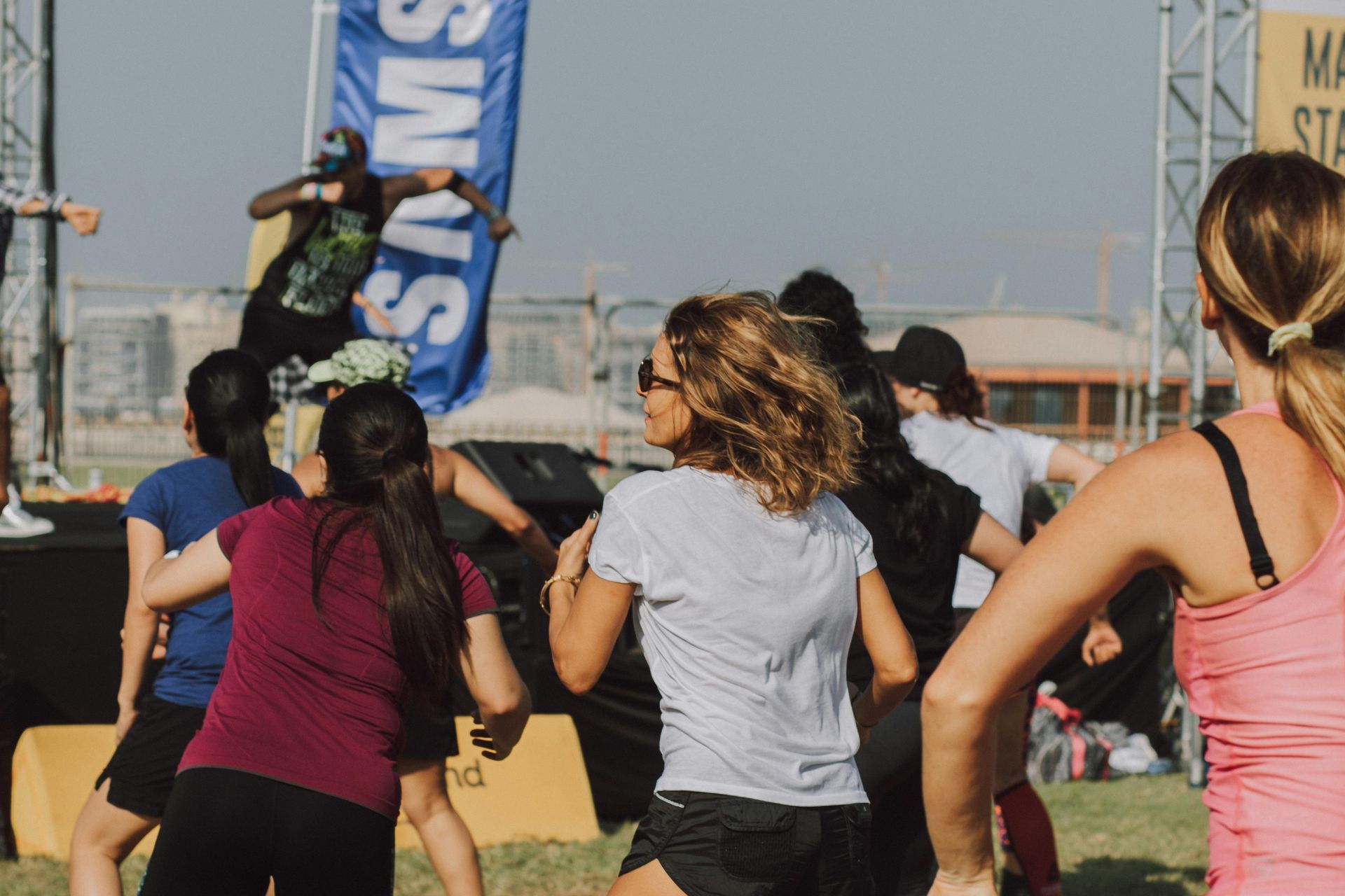 People exercising outdoors, led by a person on a stage, blue and white banner in the background.