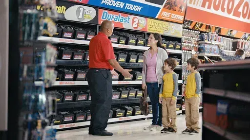Auto parts store: Employee helping a woman and two children select a car battery.