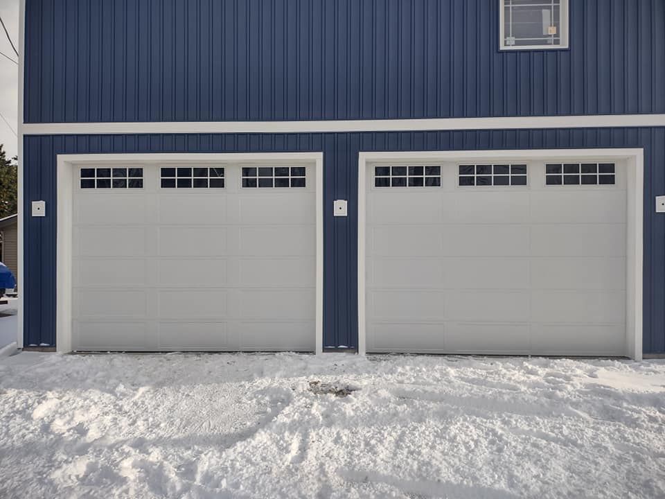 A blue garage with two white garage doors in the snow