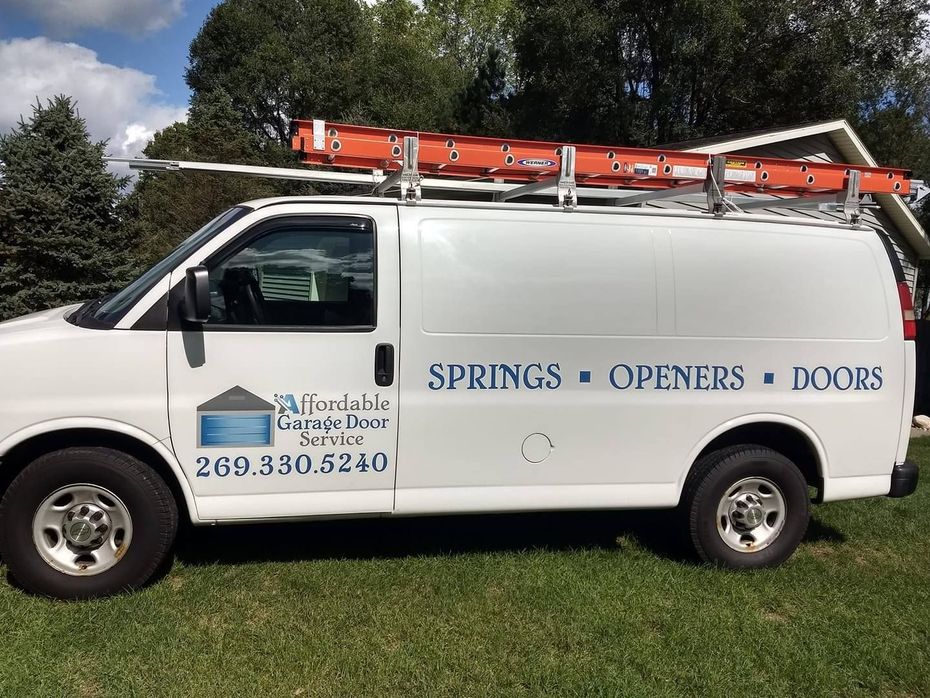 A white van with a ladder on top of it is parked in the grass.