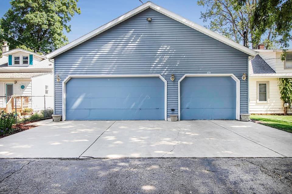 A blue garage with two blue garage doors is in front of a house.