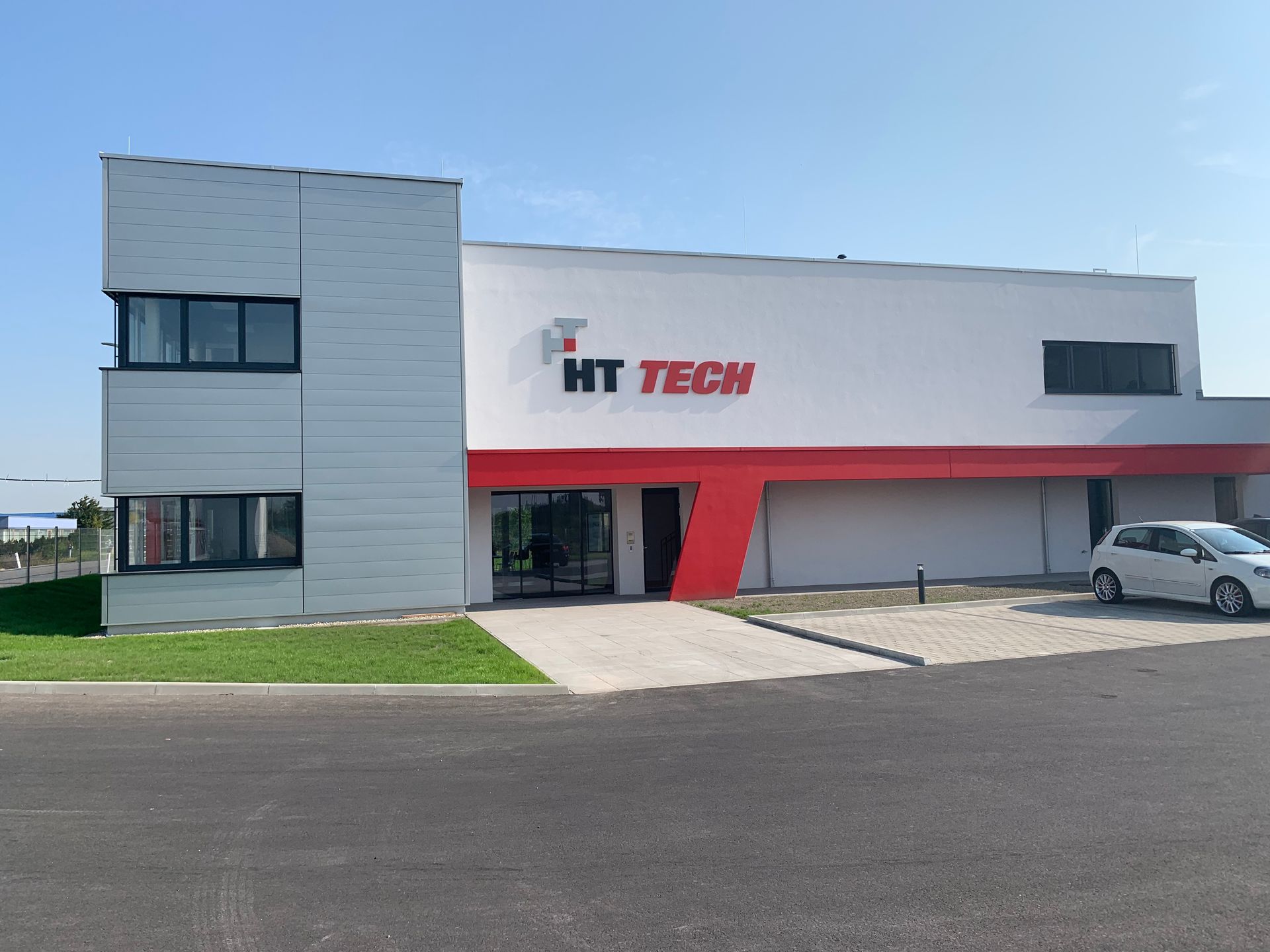 Ein weißes Auto steht vor einem Gebäude mit der Aufschrift ht tech