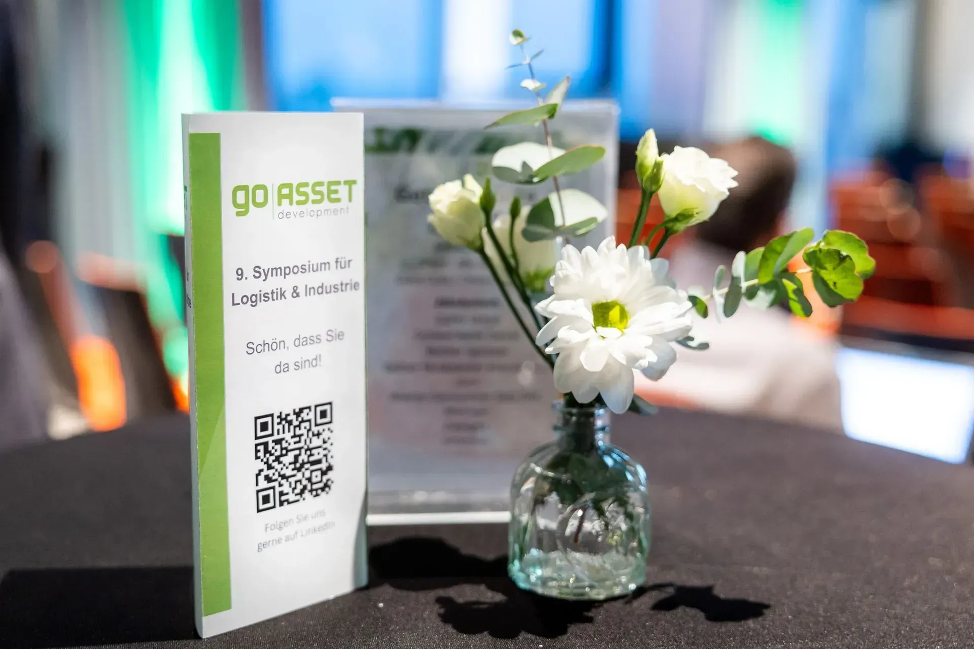 Auf einem Tisch steht eine Vase mit Blumen neben einem Schild mit der Aufschrift „Go Asset“.