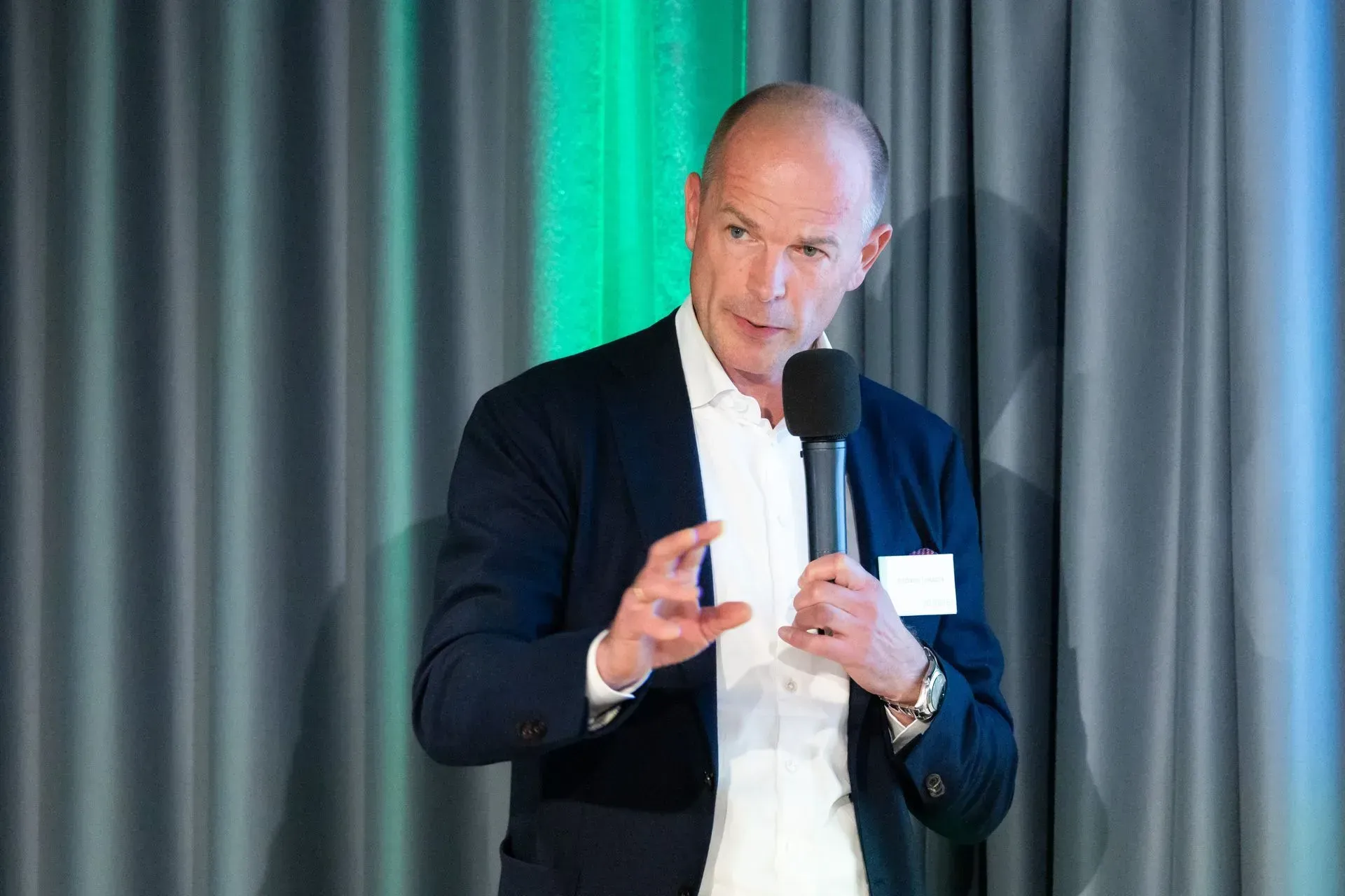 Ein Mann im Anzug hält ein Mikrofon und hält eine Rede.