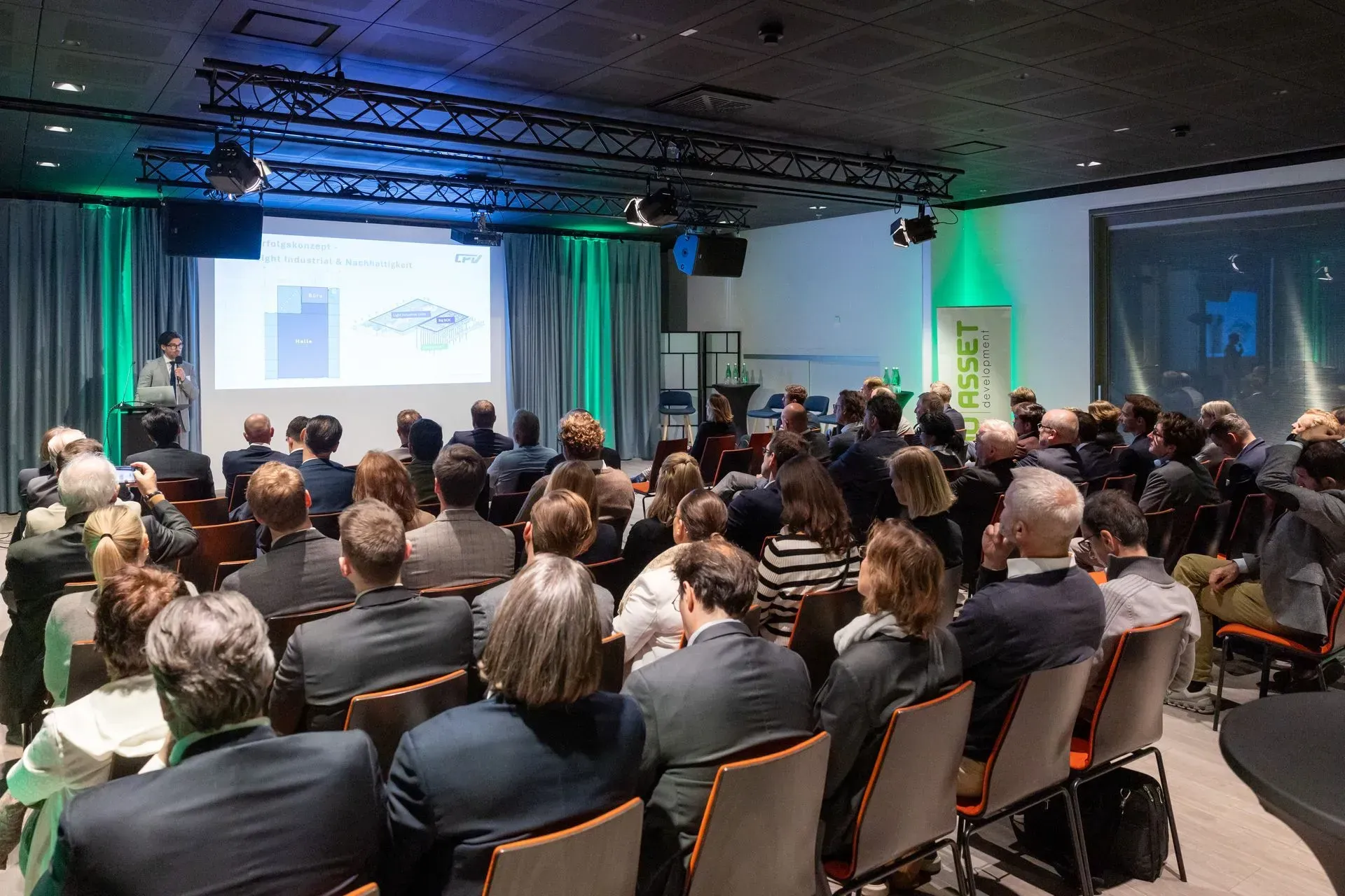 Eine große Gruppe von Menschen sitzt in einem Konferenzraum und sieht sich eine Präsentation an.