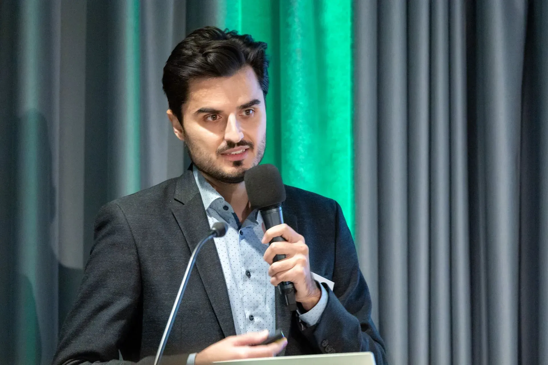 Ein Mann im Anzug steht an einem Podium und hält ein Mikrofon.