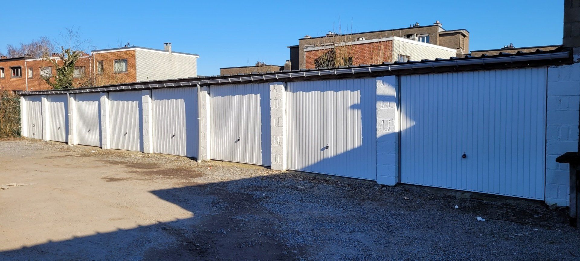 Une rangée de portes de garage blanches est alignée sur un parking.