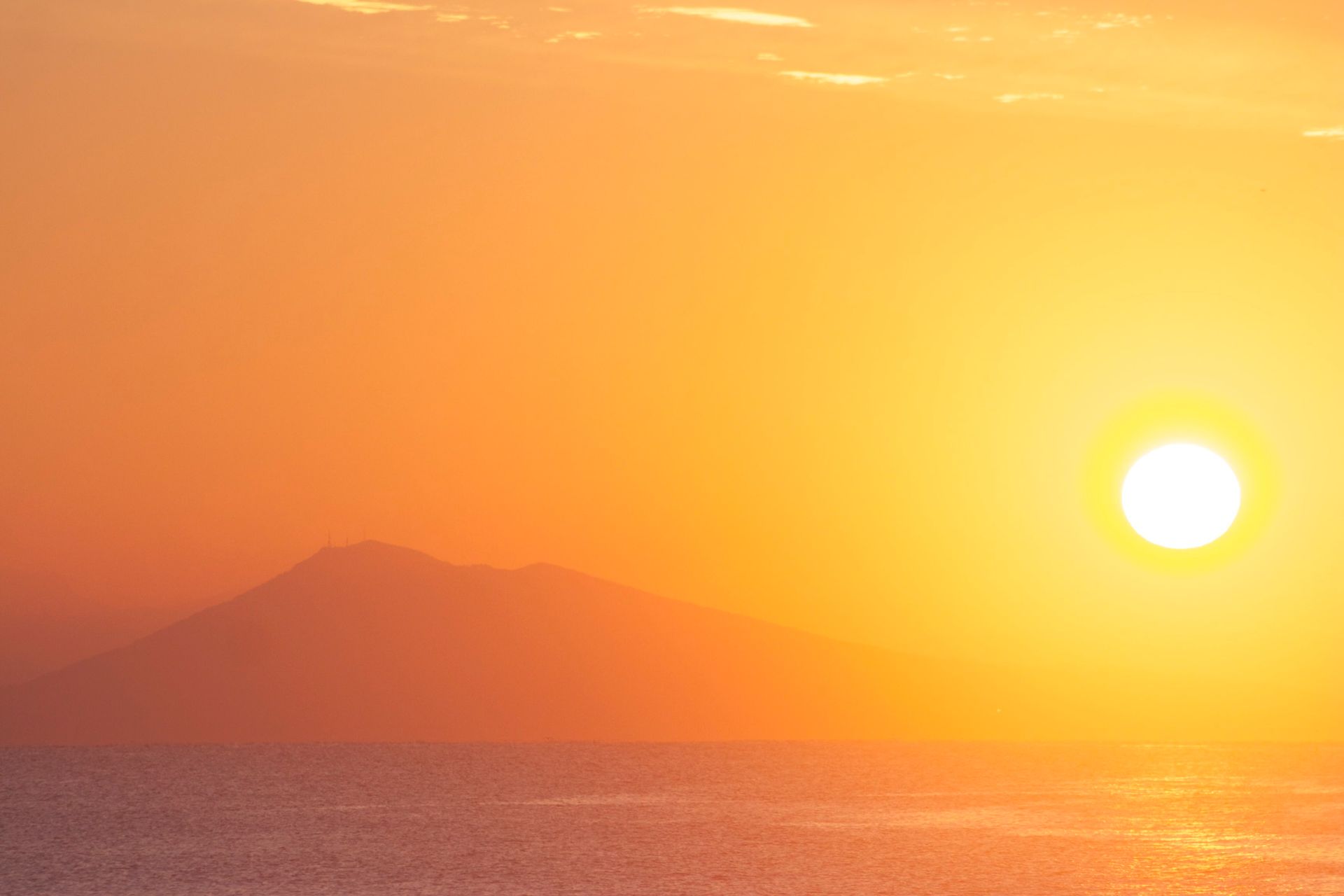 The sun is setting over the ocean with a mountain in the background.