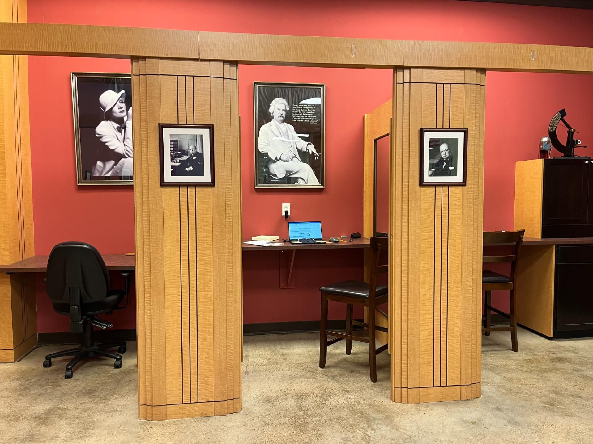 A room with two desks and chairs and two pictures on the wall.