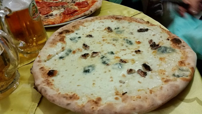 Due pizze su un tavolo, una pizza bianca con formaggio davanti e una pizza rossa dietro, con le bevande nelle vicinanze.