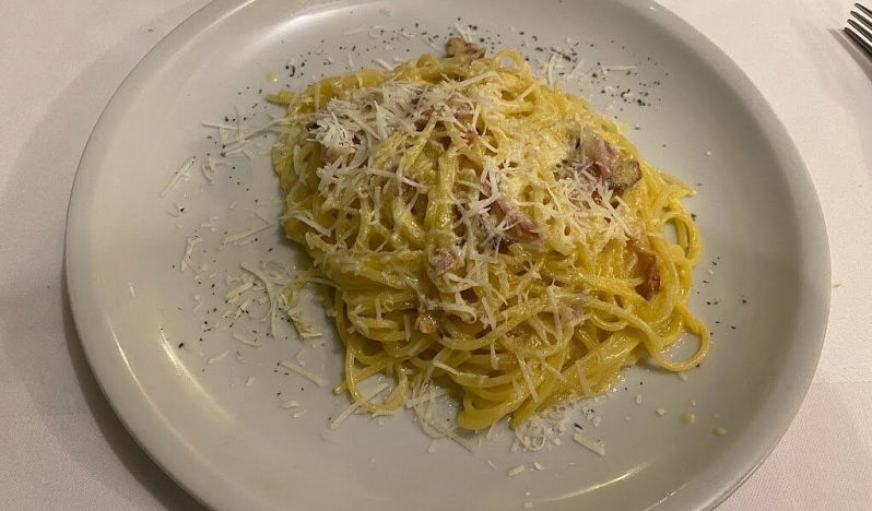 Piatto di spaghetti alla carbonara con formaggio grattugiato su un piatto bianco.