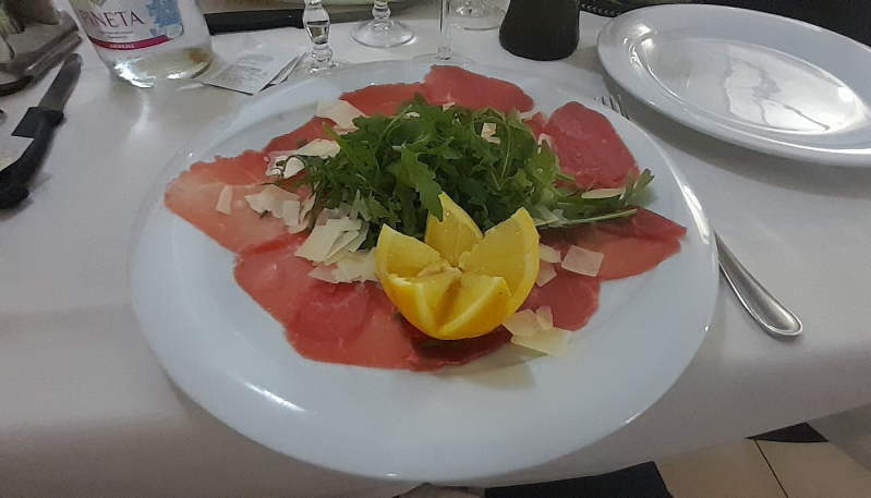 Antipasto di salmone con verdure e guarnizione di limone su un tavolo da pranzo bianco.