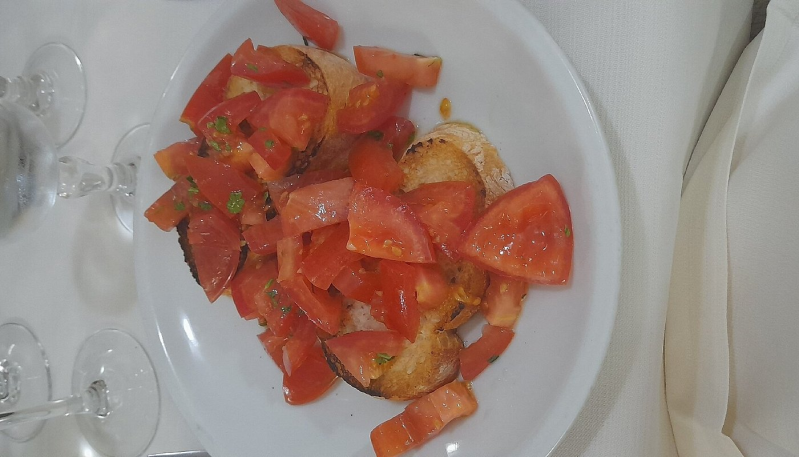 Un piatto di pomodori rossi tritati con condimento su un tavolo bianco, con bicchieri vuoti nelle vicinanze.