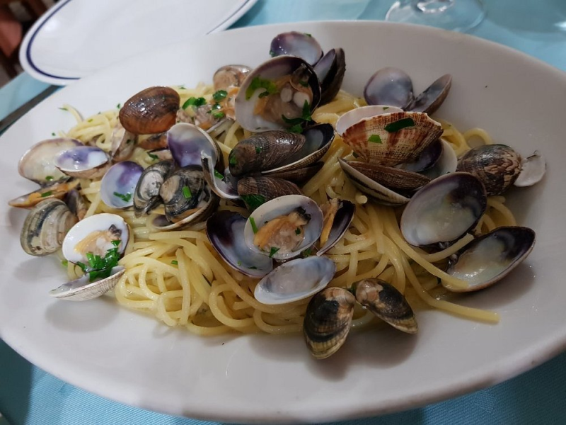 Spaghetti con conchiglie e erbe aromatiche serviti in una ciotola bianca