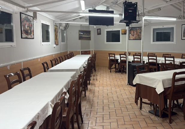 Sala da pranzo vuota di un ristorante con tovaglie bianche, sedie di legno e pavimento piastrellato.