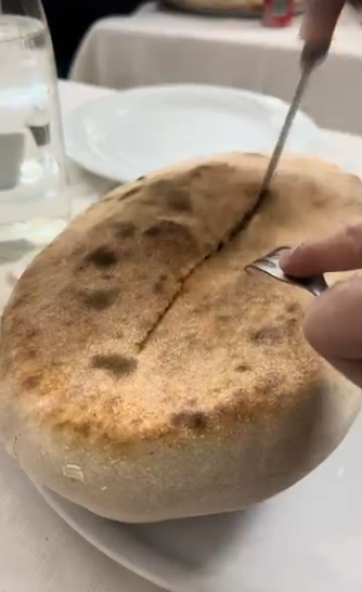 Tagliare a mano un panino dorato su un piatto bianco a un tavolo