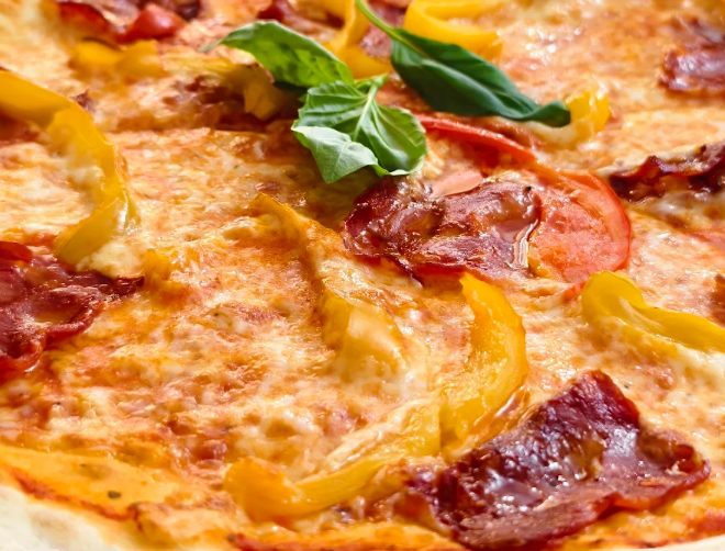 Primo piano di una pizza con formaggio fuso, salame piccante, peperoni gialli e foglie di basilico.