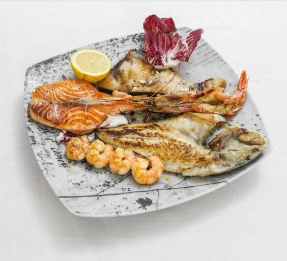 Piatto di frutti di mare grigliati con salmone, pesce, gamberi, limone e verdure su un piatto maculato.