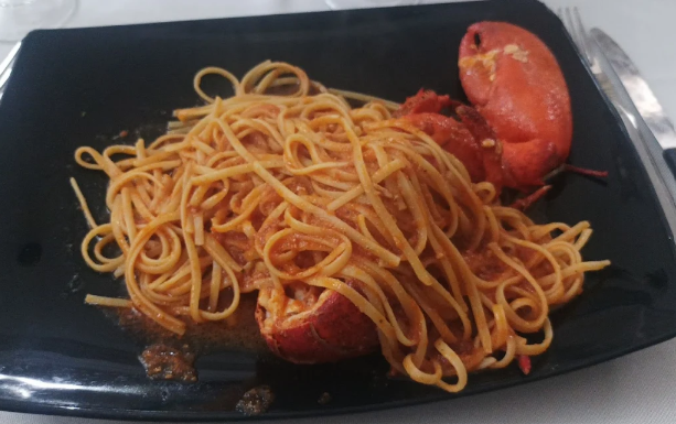 Piatto di spaghetti al sugo di pomodoro e salsiccia su un piatto rettangolare nero.