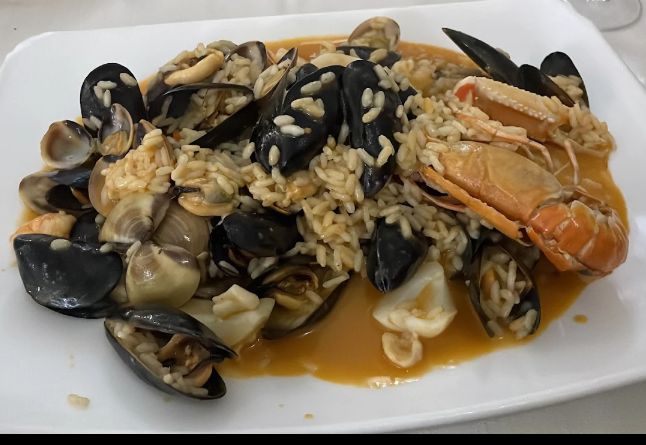 Riso ai frutti di mare con cozze, vongole e granchio in salsa marrone chiara, servito su un piatto bianco.