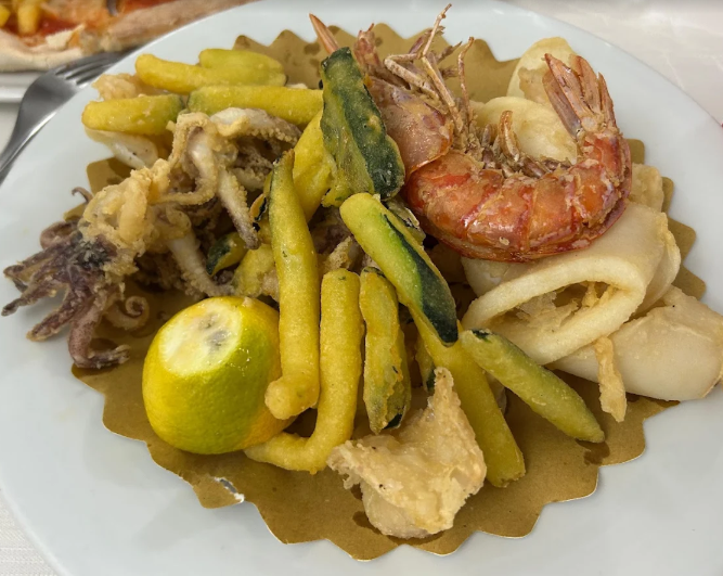 Piatto di frutti di mare con gamberi, calamari, patate e lime su un piatto bianco.