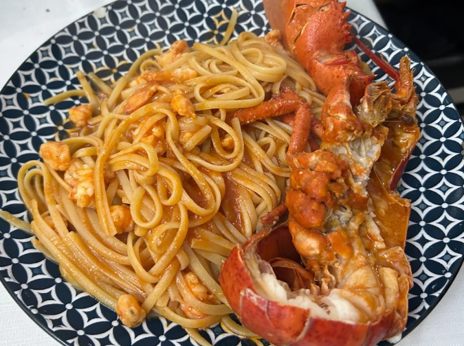 Piatto di spaghetti all'astice in salsa di pomodoro su un piatto decorato.