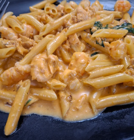 Penne cremose con gamberi e spinaci su un piatto scuro