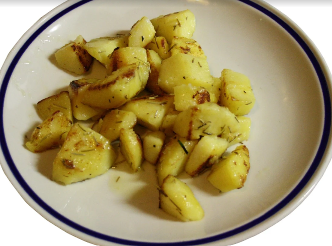 Piatto di cubetti di patate arrosto condite, serviti su un piatto bianco con bordo blu.
