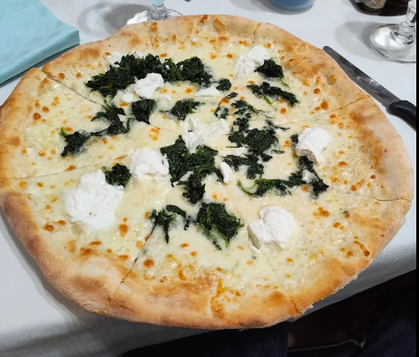 Pizza bianca con formaggio fuso e spinaci verde scuro su un piatto