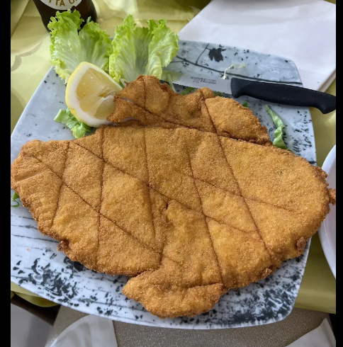 Cotoletta impanata su un piatto con spicchi di limone, guarnizione di lattuga e un coltello