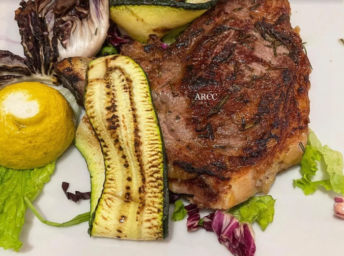 Bistecca alla griglia con verdure arrosto e lattuga su un piatto bianco.